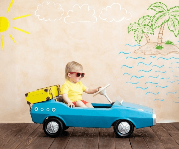 Toddler driving a blue ride-on car against a doodled summer backdrop”